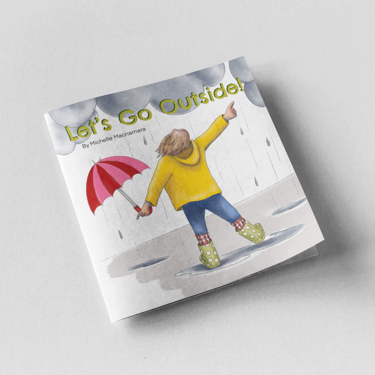 Paperback book on grey background, a rainy stormy day story called, Let’s Go Outside! by Australian Artist + Author Michelle Macnamara